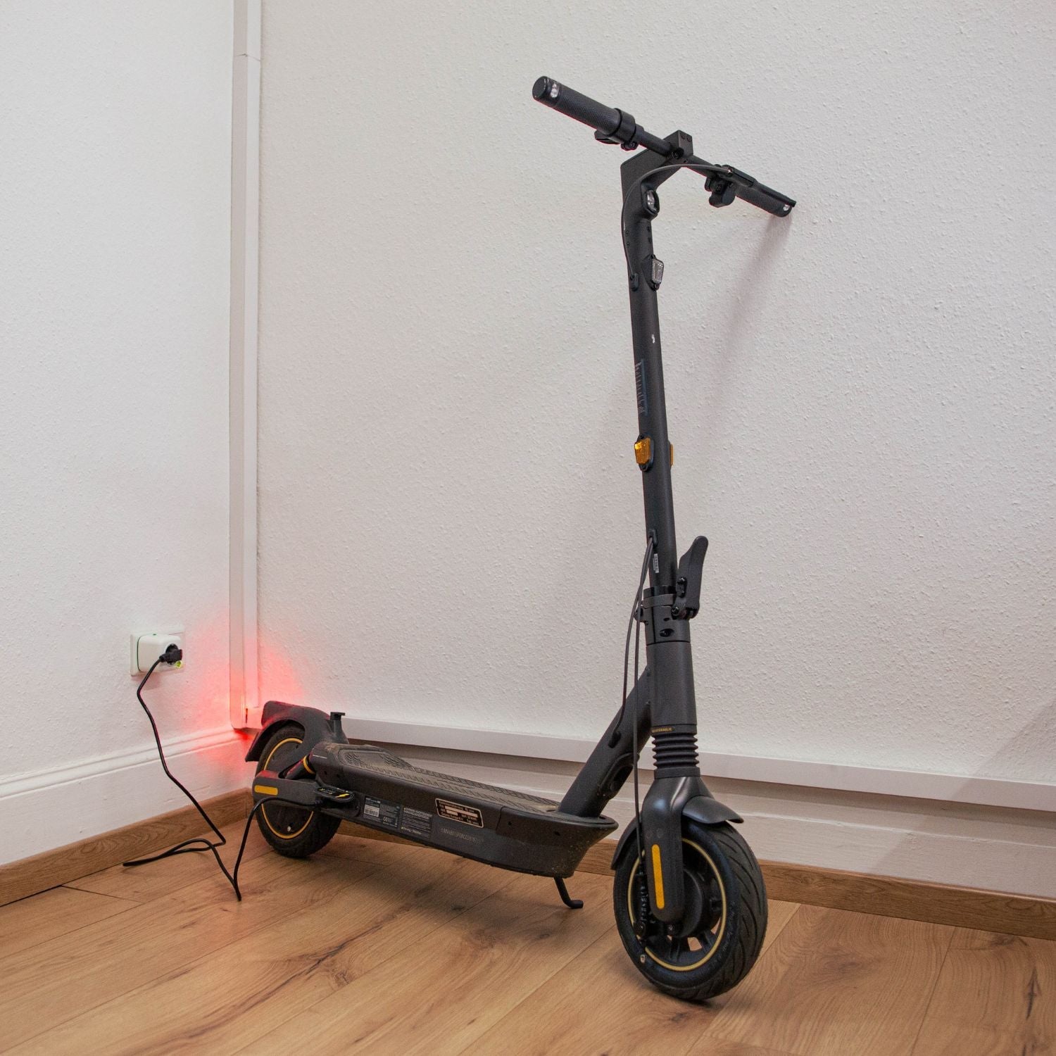 Schwarzer E-Scooter wird an der Wand geladen, Akku Life Guard sorgt für sicheres Laden, rotes Rücklicht aktiviert